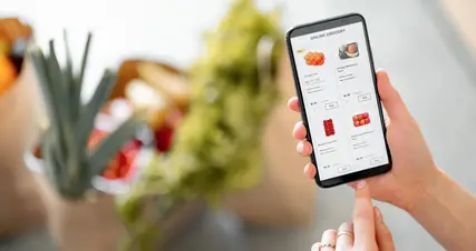 A person is holding a smartphone with a grocery app on it.