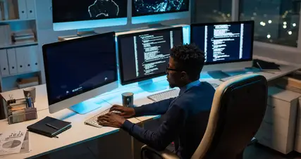 A man sitting at a desk with three monitors.