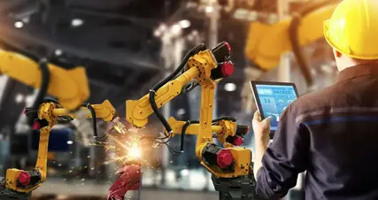 A worker is using a tablet to control a robot in a factory.